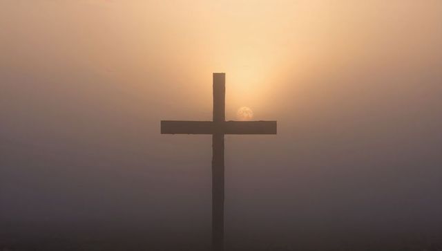 Wooden cross silhouette in misty sunrise