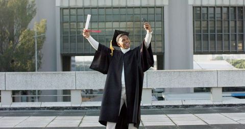 African american graduate celebrating with diploma taking selfie on campus rooftop
