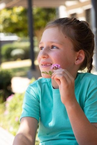 Smiling girl holding pink flowers on sunlit porch wearing teal shirt enjoying sunny garden