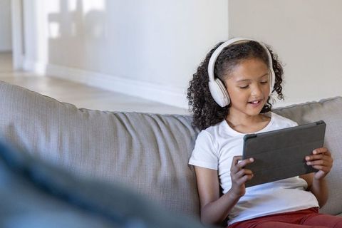 African american girl wearing headphones using tablet on sofa enjoying learning and entertainment