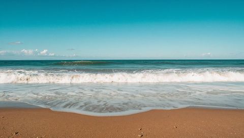 Turquoise Ocean Waves Rolling onto Sandy Shore with Foamy Surf and Wet Sand Ripples