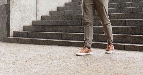 Man stepping forward on urban stone stairs wearing olive joggers and brown sneakers