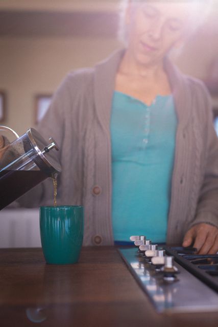 Caucasian senior woman pouring cup of coffee in sunny kitchen. retirement lifestyle, spending time alone at home.
