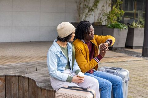 Diverse young couple checking watch while waiting with luggage in urban plaza