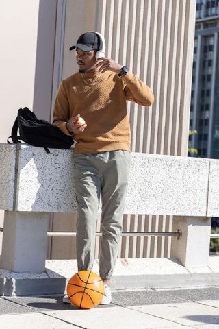 African american man listening to music on headphones leaning on rooftop with basketball