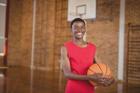 Teenage basketball player smiling in school gym holding ball