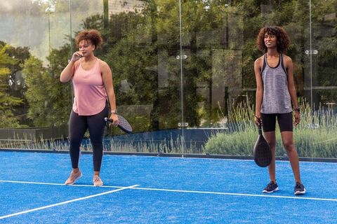 Black women playing padel on vibrant blue court holding perforated paddles wearing trackers