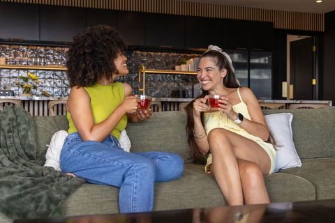 Sharing tea and laughing on sofa: two friends chatting in modern open-plan living space