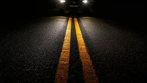 Double yellow center lines leading toward approaching headlights on wet asphalt at night