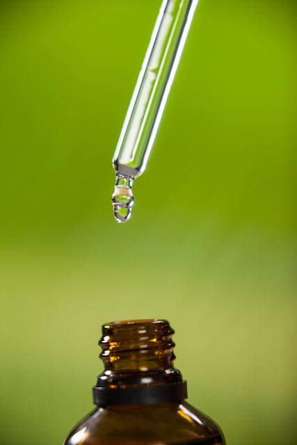 Close-up of drop of oil dripping from pipette into bottle of essential oil