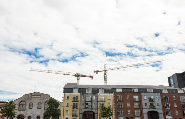 This image shows cranes at a construction site above residential buildings under a partly cloudy sky. It can be used for topics related to urban development, real estate, construction industry, city planning, and infrastructure projects.