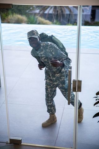 Military soldier standing by glass door with backpack on pool deck