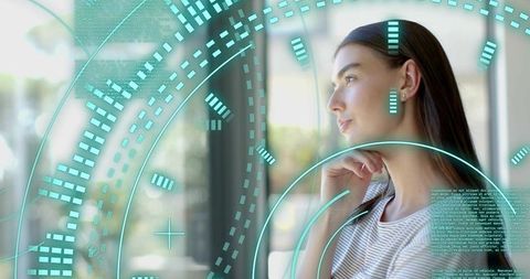 Young woman gazing through office window with teal holographic interface, contemplative