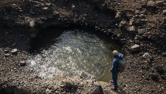 Solo hiker standing overlooking circular tide pool on rugged rocky shoreline