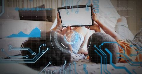 Siblings lying on bed using tablet with augmented reality overlays and laptop nearby