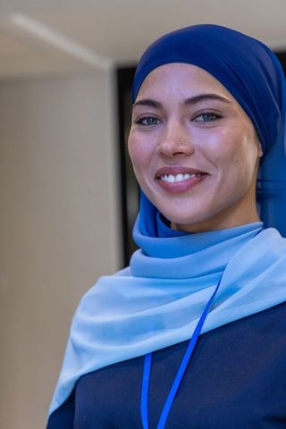 Confident young muslim professional wearing blue hijab and lanyard smiling at conference