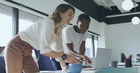 Two Women Collaborating Over Laptop in Bright Modern Office Workspace Demonstrating Teamwork
