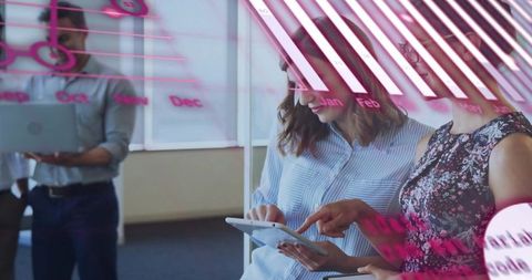 Female colleagues reviewing tablet through glass with pink calendar annotations in open-plan office