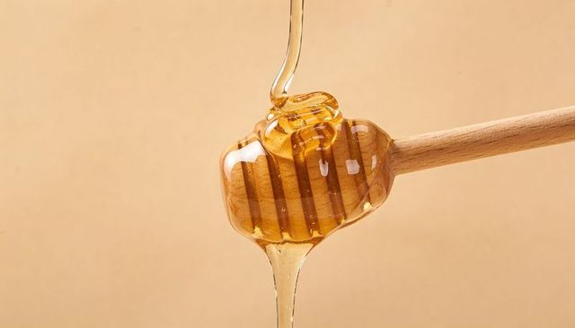 Drizzling Honey on Wooden Dipper Pouring Glossy Amber Stream with Forming Droplet