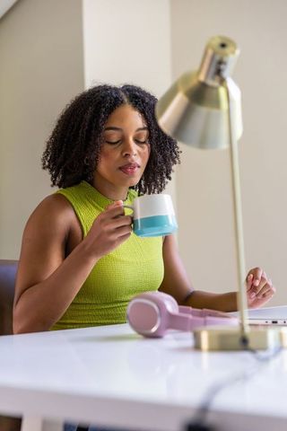 Sipping coffee while working from home woman holding turquoise mug at minimalist desk