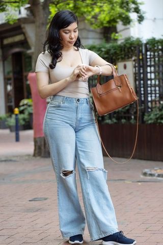 Young woman checking watch while walking urban streetstyle carrying brown leather handbag
