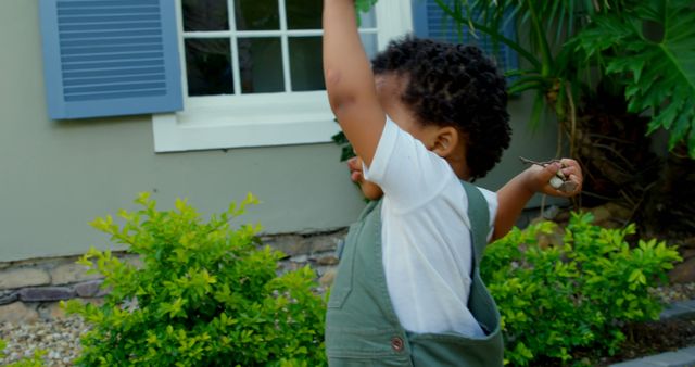 Afro toddler wearing grey overalls playing outside near window with closed shutters - Download Free Stock Images Pikwizard.com