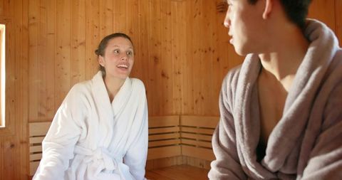 Couple relaxing and conversing in wooden sauna wearing bathrobes warm spa lifestyle