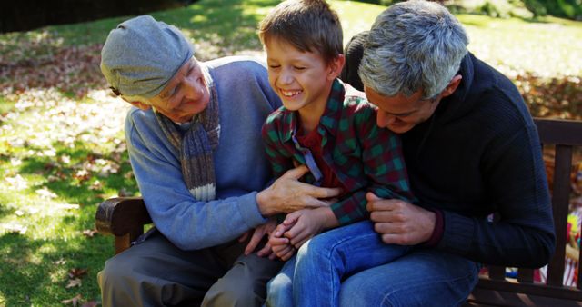 Grandfather, father, and young boy sharing a light-hearted moment sitting on a bench in a park during fall. Perfect for illustrating family bonding, outdoor activities, multi-generational relationships, and happy family moments.