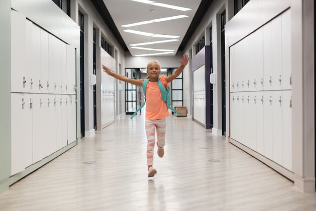 Cheerful elementary schoolgirl with arms outstretched running in a school corridor. Ideal for use in educational materials, school promotions, childhood development articles, and advertisements focusing on school supplies or children's activities.