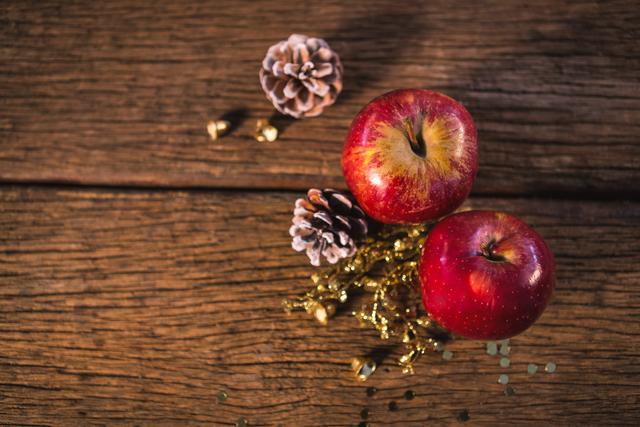 Red apples and pine cones arranged on wooden plank create a festive and rustic holiday scene. Ideal for Christmas-themed designs, holiday greeting cards, seasonal blog posts, and festive advertisements. The natural elements and wood texture add warmth and charm to any project.