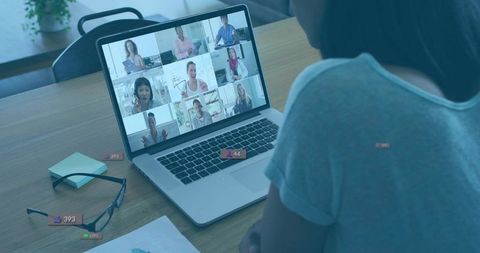 Woman joining remote team video call on laptop at home office desk with reactions and chart