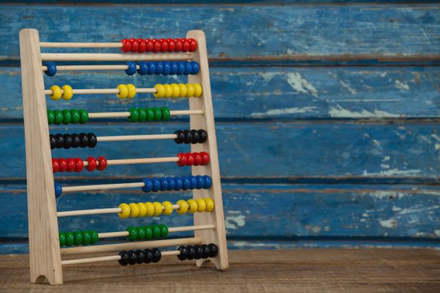 Colorful abacus with red, blue, green, yellow, and black beads on a wooden table against a blue wooden background. Ideal for educational content, children's learning materials, math tutorials, vintage-themed designs, and school-related projects.