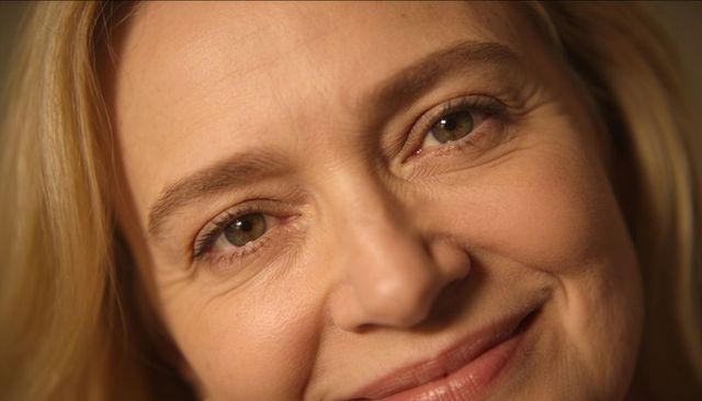 Smiling mature woman showing natural fine lines and warm skin texture closeup, blonde hazel eyes