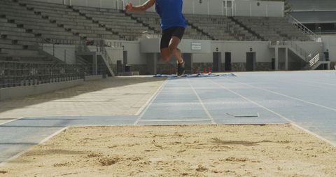 Long jumper mid-air over sand pit at stadium