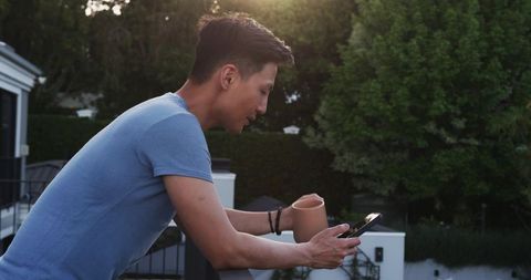 Man Relaxing on Balcony with Mug and Smartphone at Sunset