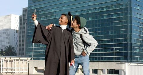 Graduate friend taking selfie on urban rooftop celebrating diploma achievement