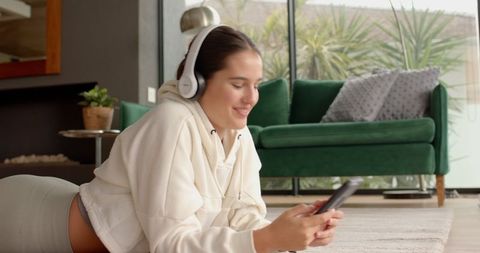 Woman Relaxing with Smartphone and Headphones on Soft Rug Indoors