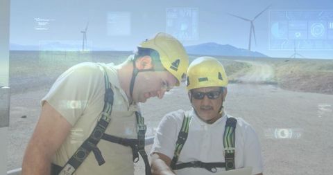 Technicians collaborating on tablet with hud overlays at wind turbines in arid plain