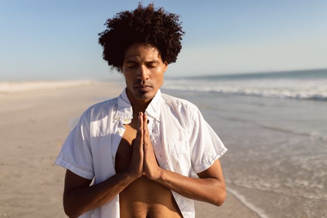 Front view of young African-american man performing yoga on the beach