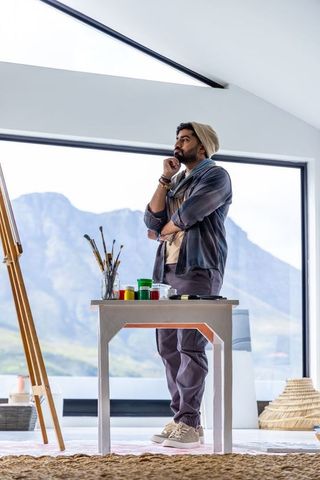 Contemplative painter standing in bright studio with mountain view and paint supplies