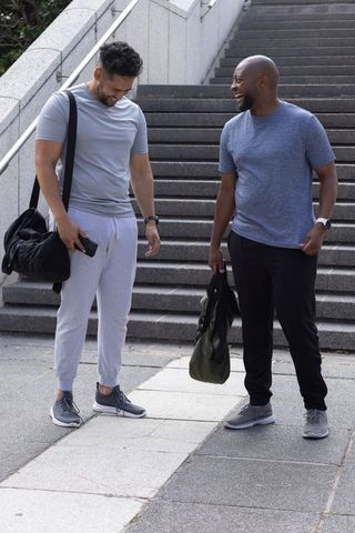 Two african american men laughing in athletic wear with gym bags on city staircase