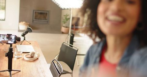 Smiling female vlogger recording at desk with microphone, tripod, lighting and headphones