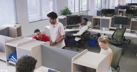 Casual team collaborating in modern open-plan office, coworkers using laptops and phone