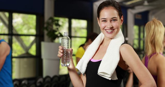 Young woman smiling, suggests post-workout satisfaction, holding a water bottle in gym. Ideal for promoting fitness, health, hydration, women's wellness programs, active lifestyles, or gym memberships.