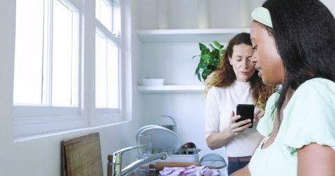 Diverse women sharing kitchen chores in bright modern apartment