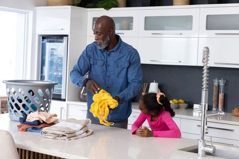 African american father folding laundry with daughter in modern white kitchen island