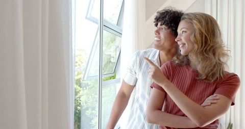 Happy Couple Enjoying View Through Large Window in Modern Living Room