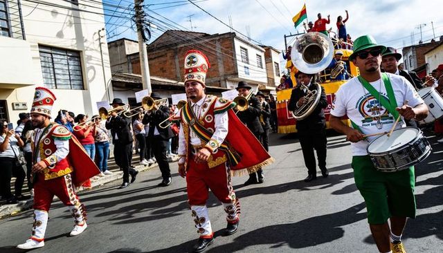 Marching carnival band playing brass and drums with colorful float and street spectators