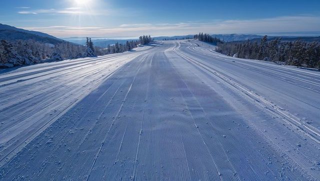 Sunlit corduroy ski run stretching to mountain ridge at dawn with groomed tracks