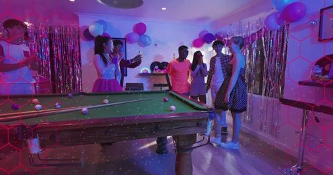 Friends celebrating around pool table under neon lights with balloons and streamers